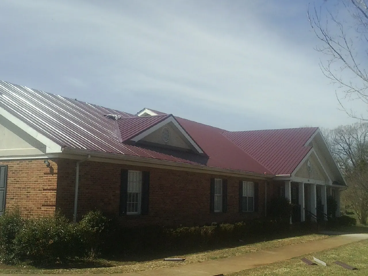 Red metal roof with gabled entries on a long brick building, from a Hail Damage Roof Repair job in Colora