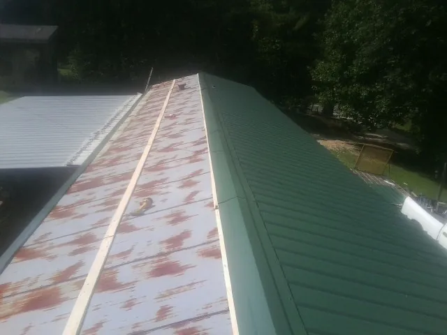 Old rusted panels beside newly installed green metal roofing — Wind Damage Roof Repair by Roofing Brothers in Colora