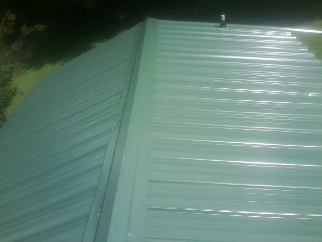 New green metal panels meeting at the ridge of a roof — Flat Roof Repair work by our crew in Colora