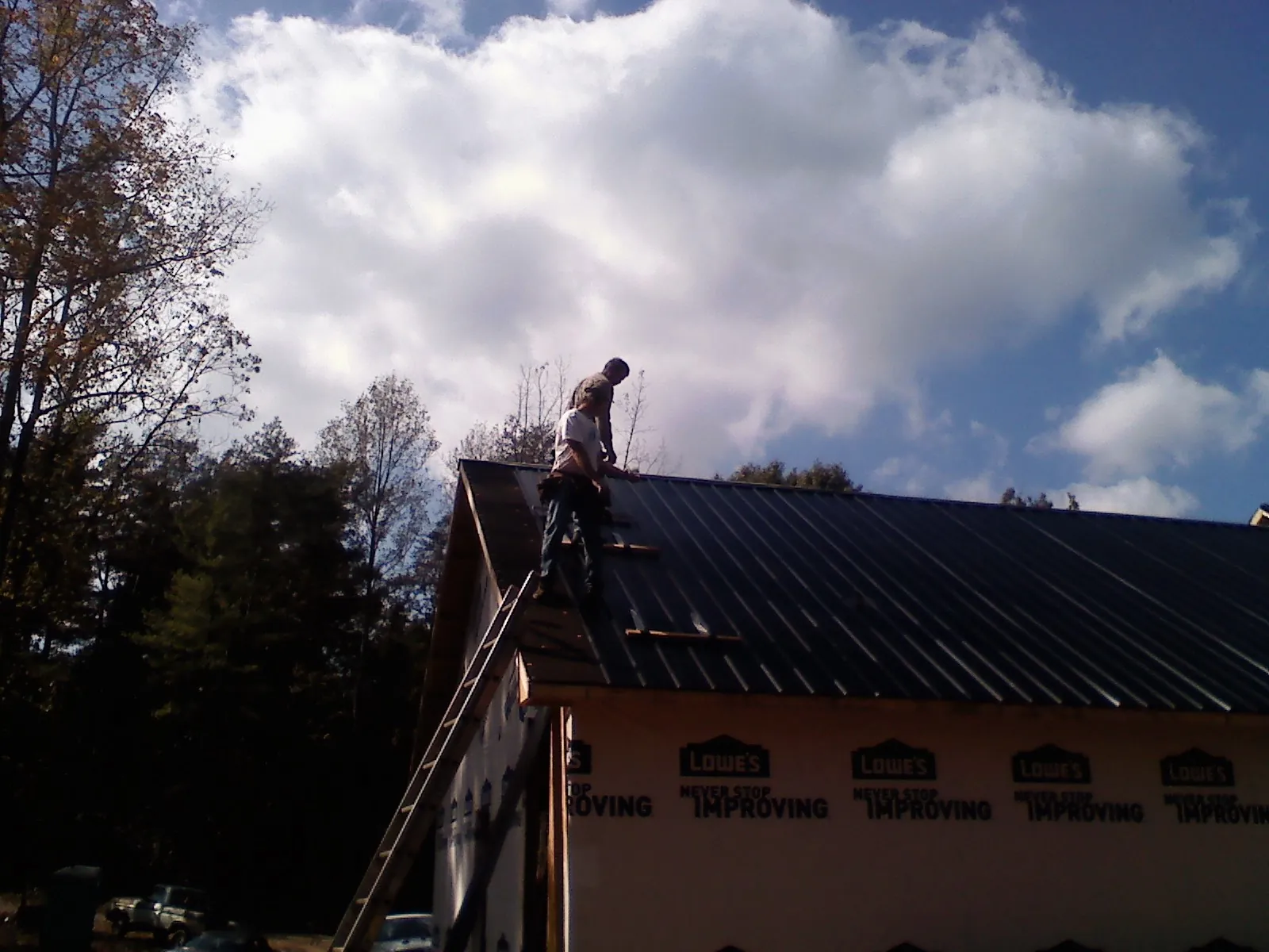 Roofer fastening dark metal panels high against a cloudy sky, from a Roof Inspection job in Colora